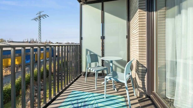 A balcony with two chairs and a table, a sliding glass door, and a view of a building and antenna. - Nadmotławie 75 | Riverside | Sauna & Gym (Gdańsk)