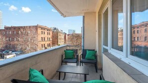 Een balkon met een tafel en stoelen, een uitzicht op gebouwen en een heldere lucht.