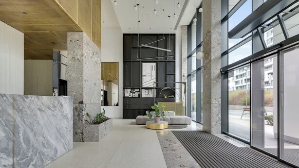 Un hall d’entrée moderne avec un comptoir de réception en marbre, un espace salon avec des canapés et de grandes fenêtres offrant une vue sur l’extérieur.