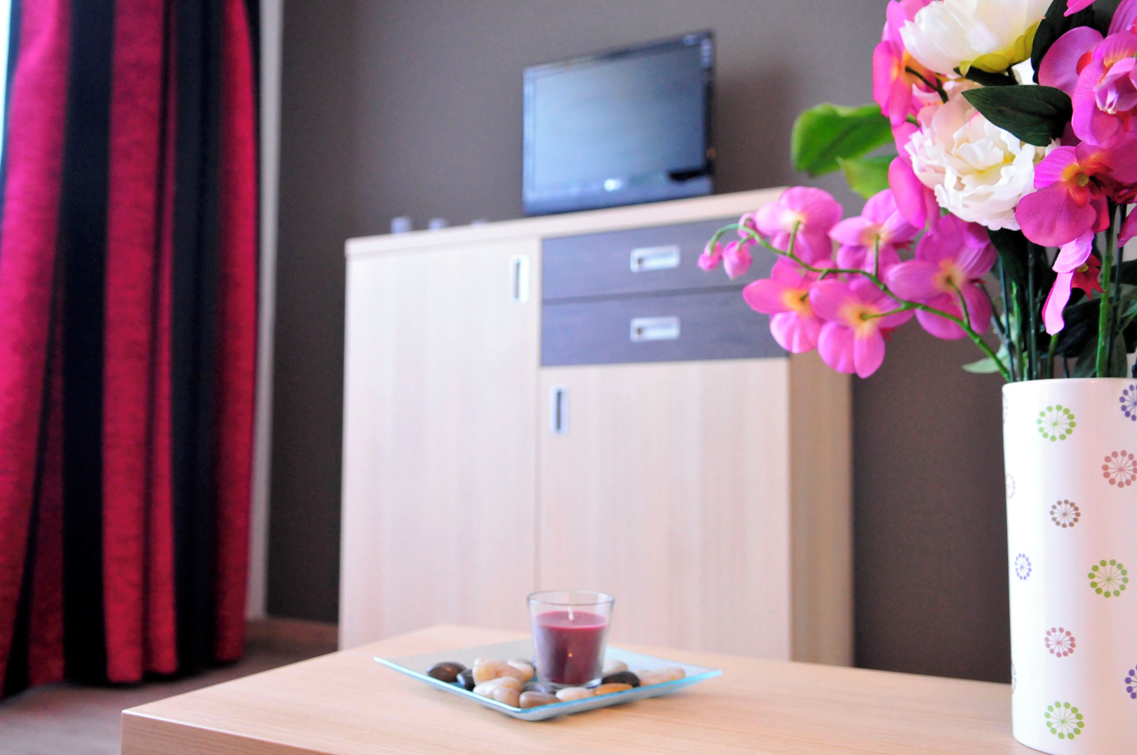 A room with a wooden cabinet, a glass of drink on a plate, and a vase with flowers.