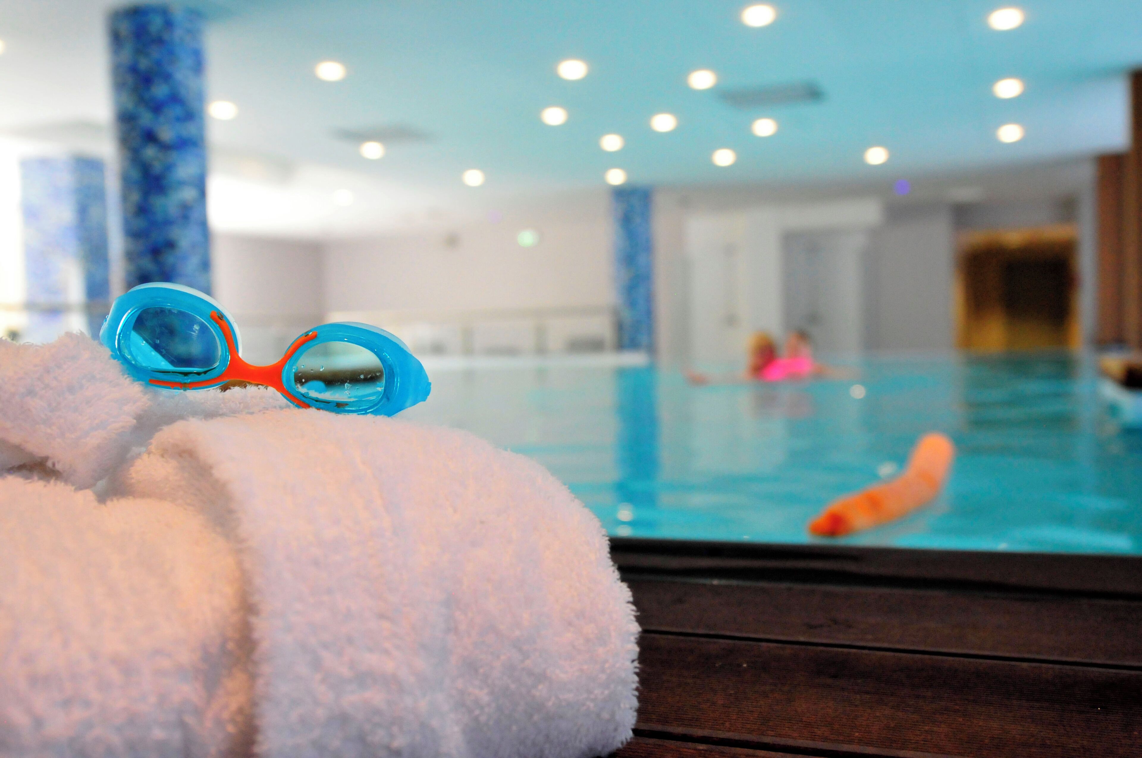 A pool area with a towel and goggles, a person swimming, and a carrot in the water.