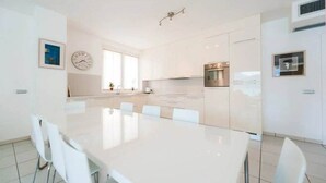 A modern kitchen with white cabinetry, a stainless steel oven, and a dining area with a white table and chairs. - Stunning 4br/3ba Italian Lakes Apt in a Beautiful Lakeside Setting (Maccagno con Pino e Veddasca)