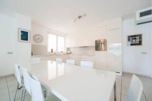 Eine moderne Küche mit weißen Schränken, einem Edelstahlbackofen und einem Essbereich mit weißem Tisch und Stühlen.
