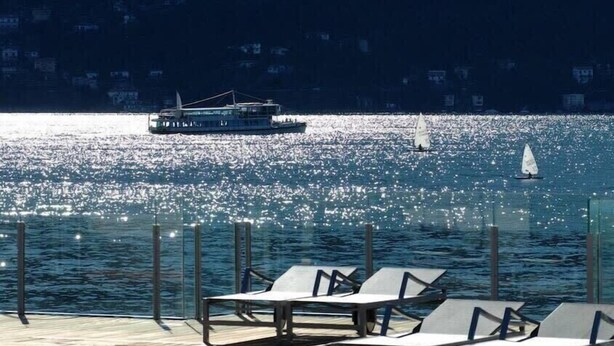 A waterfront area with lounge chairs, a boat, and a sailboat on the water. - Stunning 4br/3ba Italian Lakes Apt in a Beautiful Lakeside Setting (Maccagno con Pino e Veddasca)