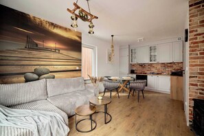 Ein modernes Wohnzimmer mit einer Couch, runden Tischen und einer Küche mit weißen Schränken und einer Ziegelwand.
