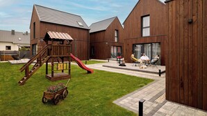 A modern building with a wooden exterior, a play area with a slide, and a paved patio. - Sunset Wood Resort 4 | Jacuzzi | Parking (Jastrzębia Góra)