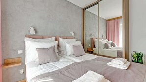 Quarto de hotel moderno com uma cama grande, abajures, um espelho e uma pequena planta.