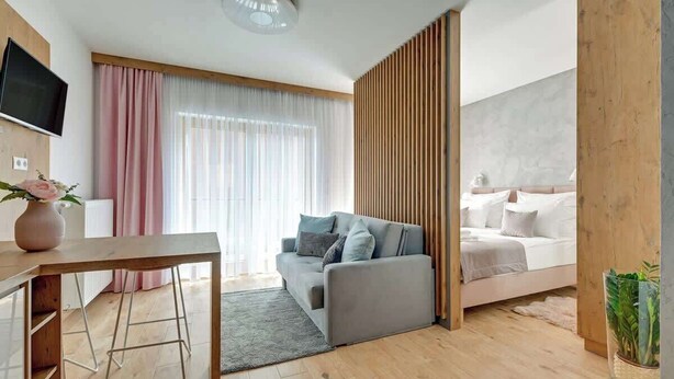 Quarto de hotel moderno com sofá, cama, televisão e divisória de madeira.