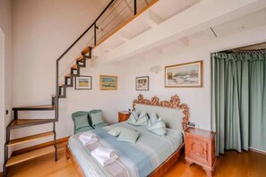 Un dormitorio con cama, mesita de noche, silla, escalera y ventana con cortinas.
