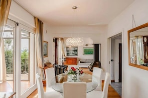 Una sala de estar moderna con una mesa de comedor de vidrio, sofás blancos y una araña.