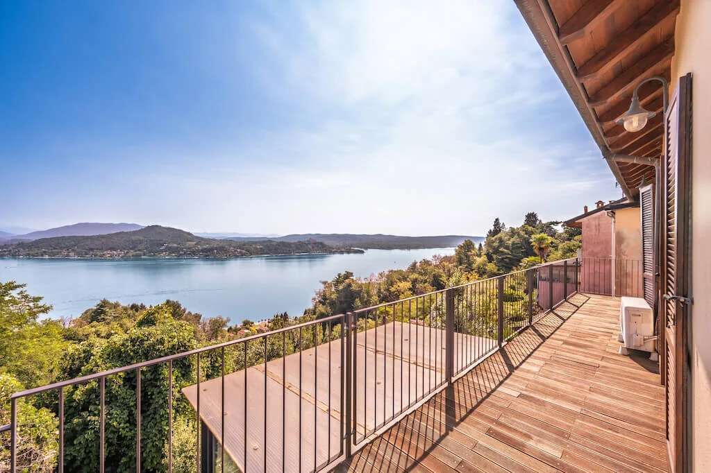 A wooden deck with a metal railing overlooking a lake and hills.