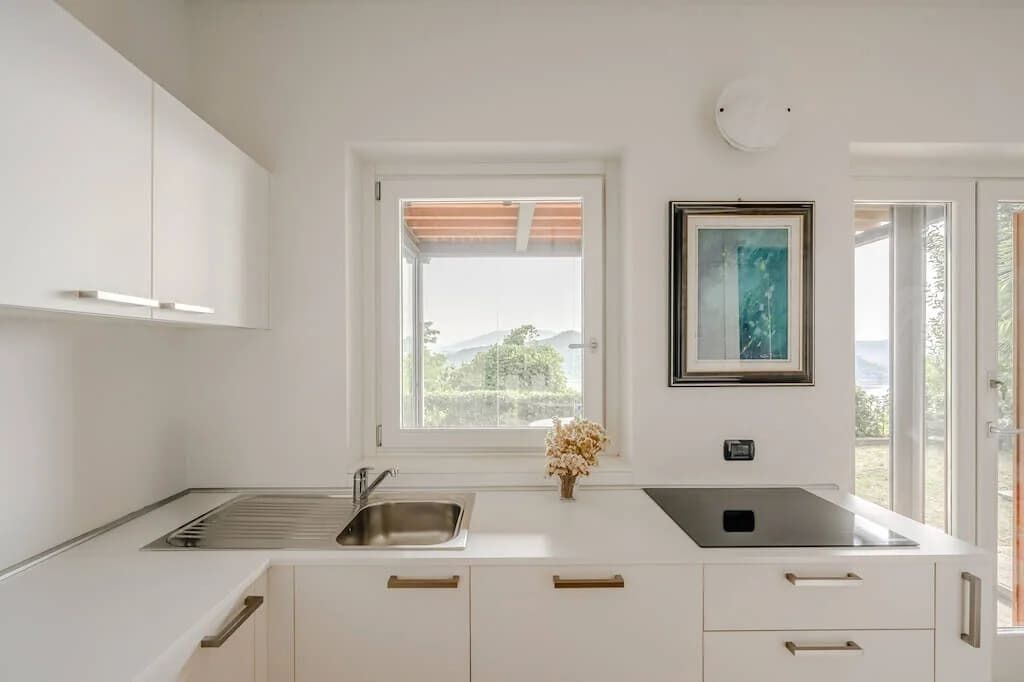 A modern kitchen with white cabinetry, a stainless steel sink, and a window with a view of greenery.