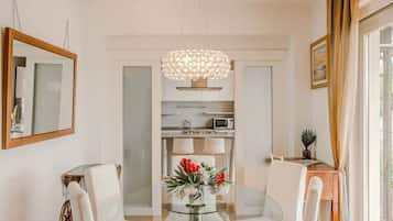 A dining area with a glass table, white chairs, a chandelier, and a vase with flowers.