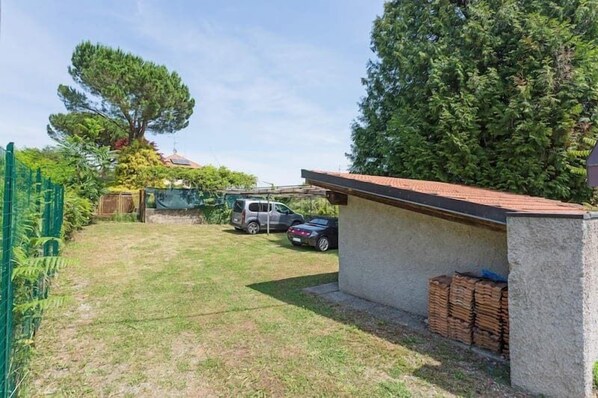 A fenced backyard with a small building, parked cars, and a large tree.