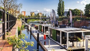 Ein modernes schwimmendes Restaurant mit Außenbereich, Blick auf den Fluss und einer Brücke im Hintergrund.