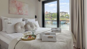 Ein Hotelzimmer mit einem großen Bett, einem Gemälde, Blick auf ein Gewässer und die Stadt.