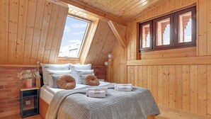 Ein Schlafzimmer mit Holzwänden und schrägen Decken, einem Bett mit Kissen und Decke, einem Nachttisch und einem Fenster mit Aussicht.