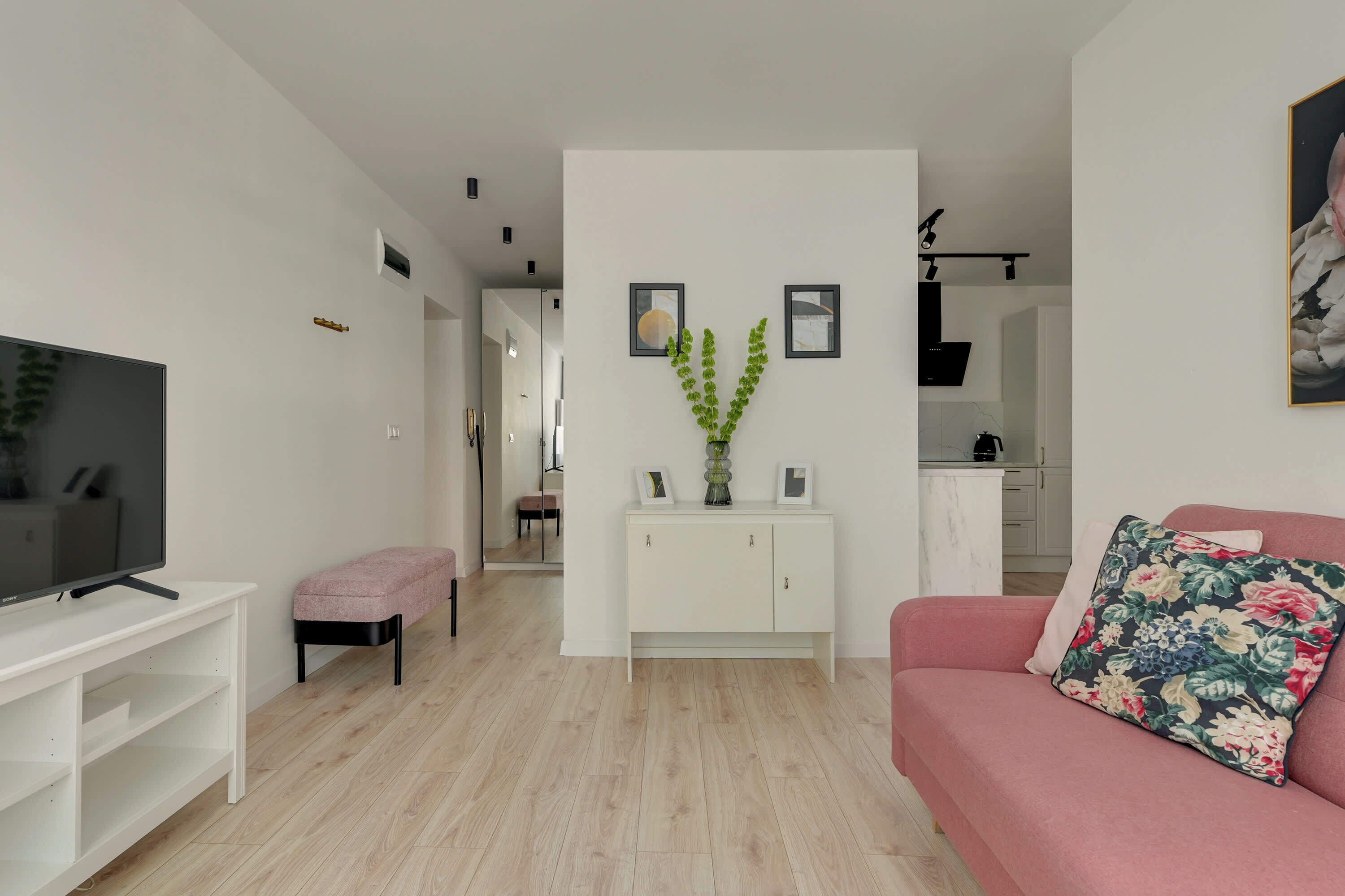 Una sala de estar moderna con un televisor de pantalla plana, un sofá rosa, una consola blanca y una planta verde.