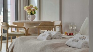 Ein Hotelzimmer mit einem Bett, zwei Stühlen, einem Tisch mit Blumenvase, zwei Gläsern Wasser und Handtüchern mit Aufdruck.