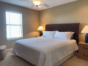 A bedroom with a bed, a nightstand, a lamp, a ceiling fan, and a window. - Lagoon Front Paradise with Beach Access (Gulf Shores)
