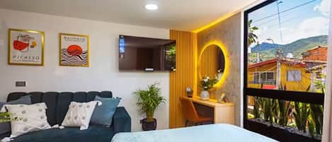 Ein modernes Zimmer mit Sofa, Bett, Fernseher, Spiegel und Bergblick.
