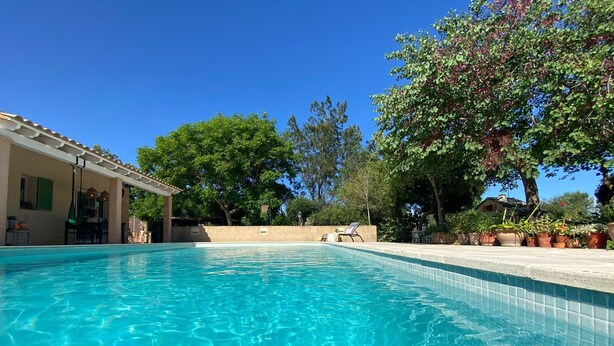A clear swimming pool with a tiled edge, surrounded by a patio area with potted plants and a pergola. - Welcome to C'an Felip in Artà (Artà)