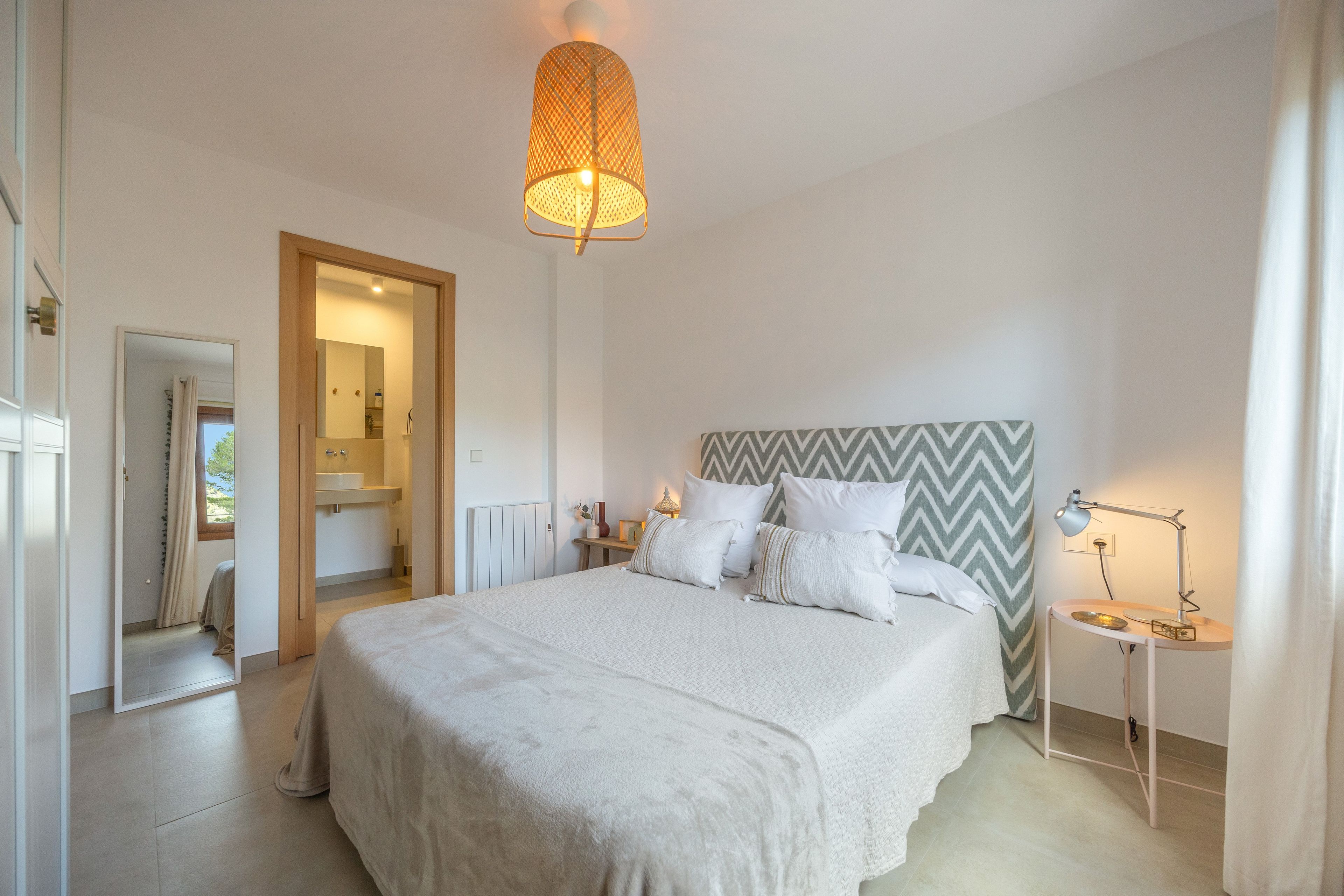 Un dormitorio con cama, lámparas de noche, un espejo y una puerta que da a un baño.