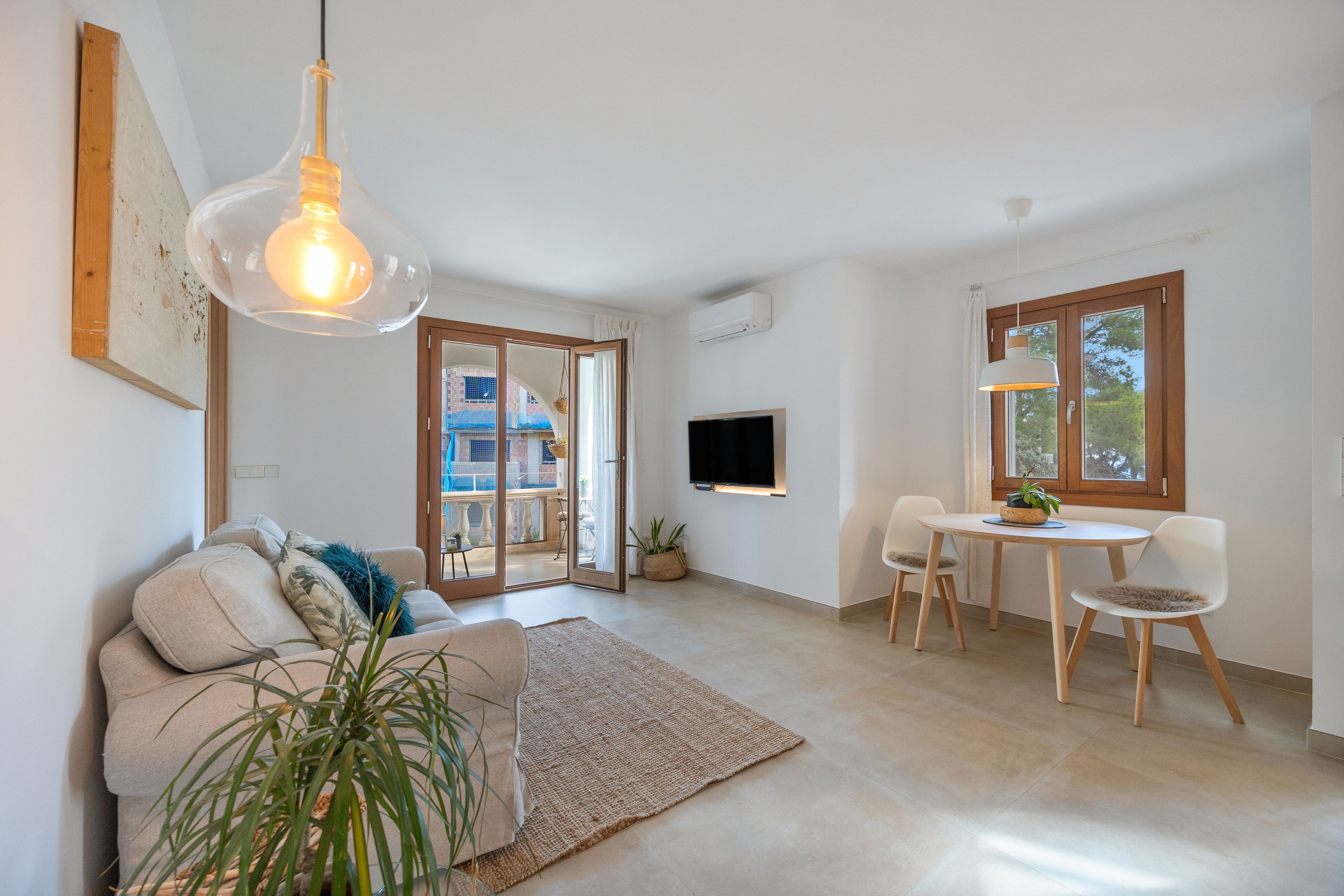 Una sala de estar moderna con un sofá, una mesa de comedor con sillas, un televisor montado en la pared y un ventanal grande.