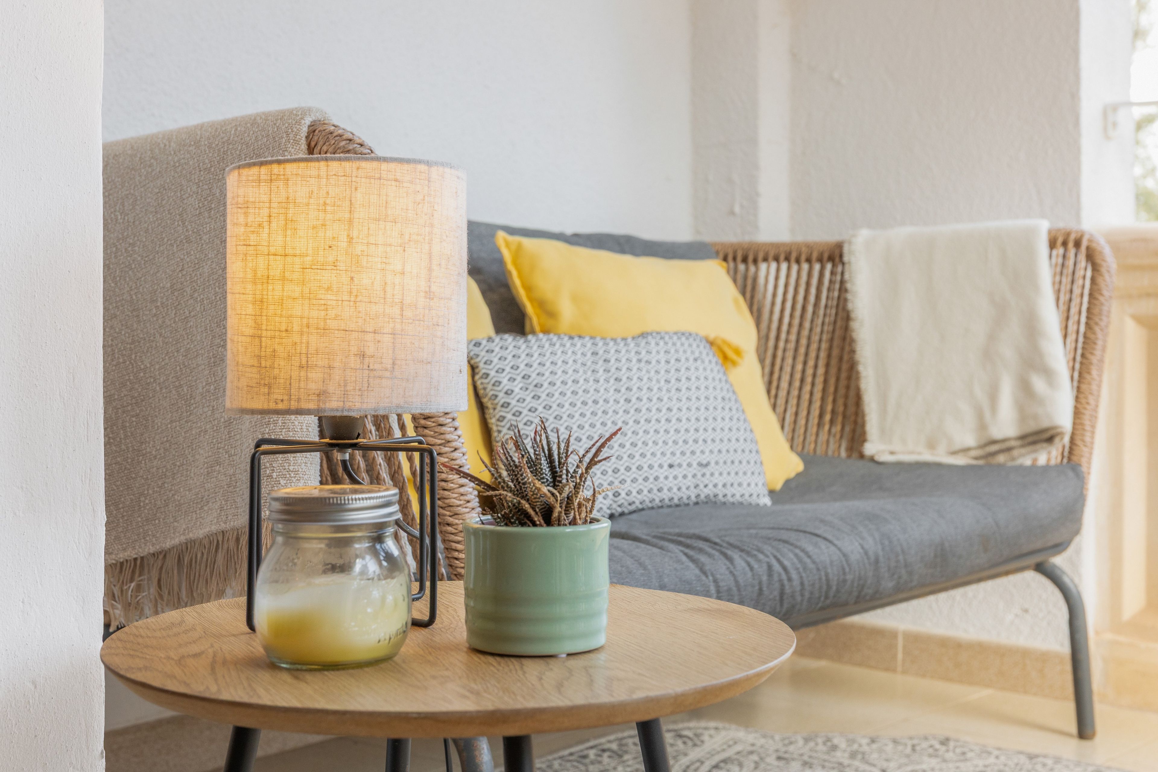 Un rincón acogedor con sillones, una lámpara, una mesita con un frasco y una planta, y un cojín con almohada amarilla.