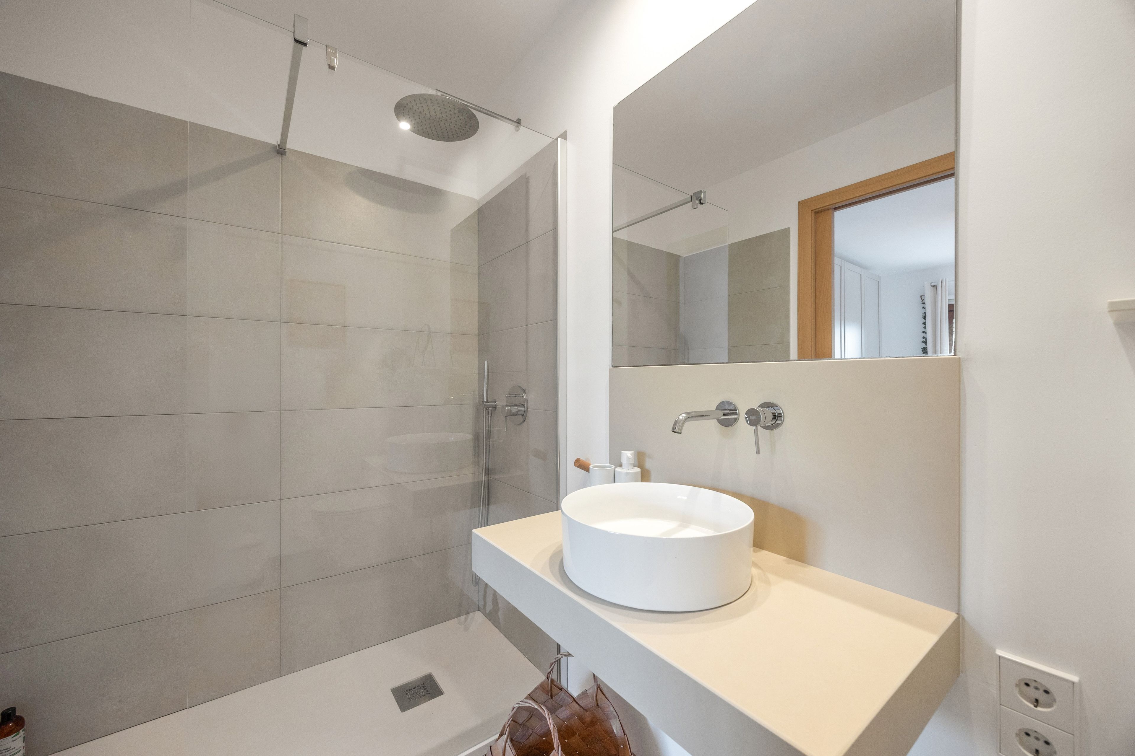 Een moderne badkamer met een inloopdouche, een rond wastafel en een spiegel boven de wastafel.