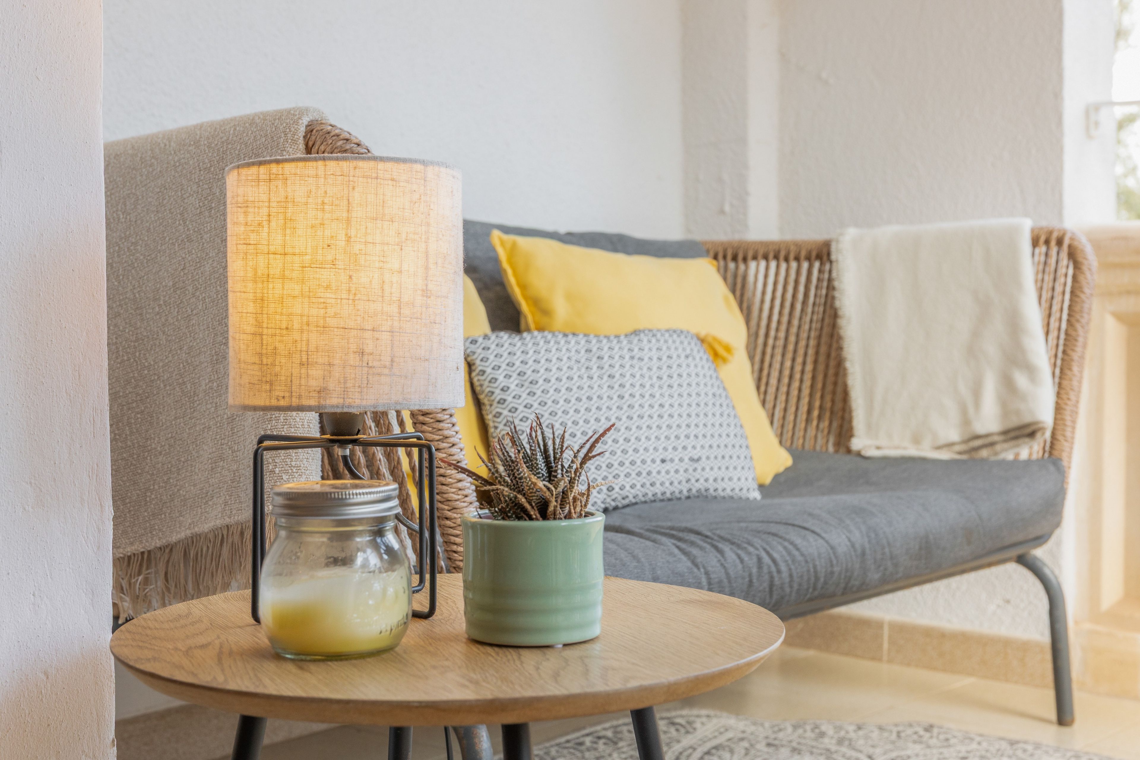 Un coin salon accueillant avec une table ronde en bois, une lampe, un bocal en verre et une plante en pot.