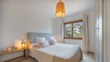 Un dormitorio con una cama, una mesita de noche, un reloj de pared, una ventana y una lámpara colgante.