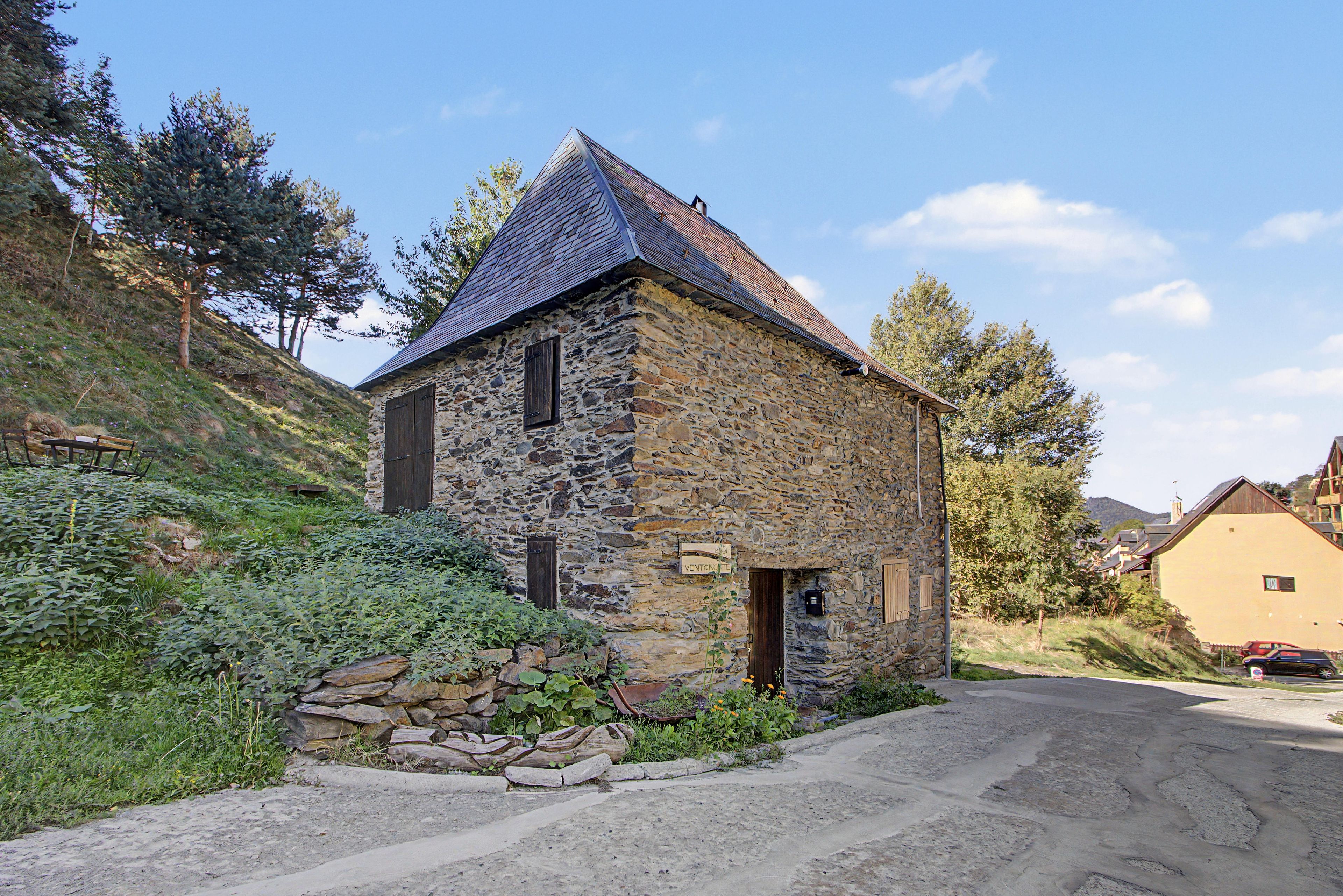 A stone building with a sloped roof, a wooden door, and a sign indicating its name.