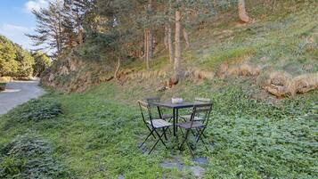 A table and chairs set up on a grassy slope with a road and trees in the background.