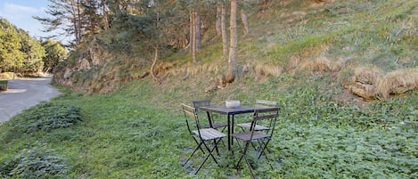 Una mesa y sillas dispuestas en una ladera cubierta de césped, con un camino y árboles al fondo.