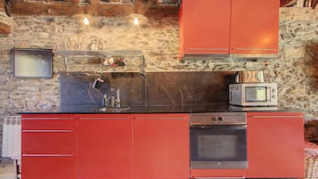 Een keuken met rode kasten, een zwart aanrecht, een magnetron en een fornuis.