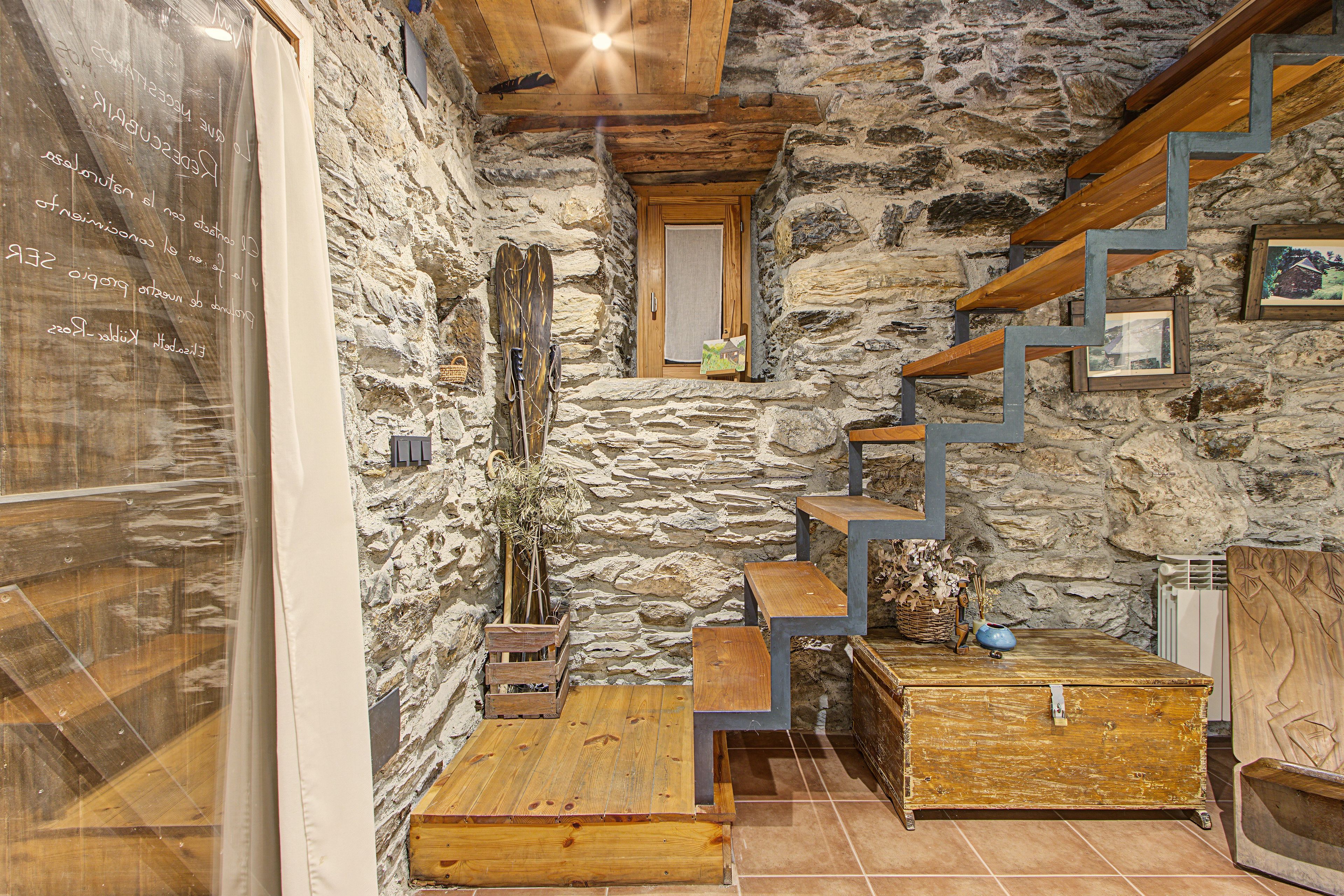 Un intérieur rustique en pierre, avec un escalier en bois, une petite fenêtre et un coffre en bois.