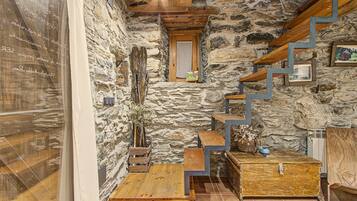 Un intérieur rustique en pierre, avec un escalier en bois, une petite fenêtre et un coffre en bois.