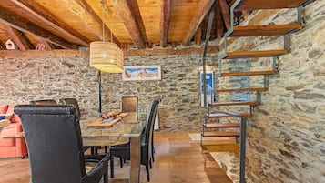 Un interior rústico con pared de piedra, escalera de madera y un comedor con mesa y sillas.