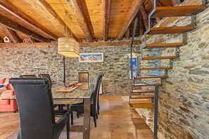 A rustic interior with a stone wall, wooden staircase, and a dining area with a table and chairs.