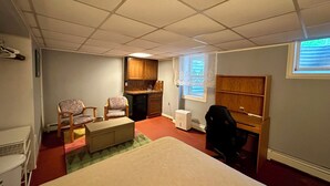 A compact room with a bed, a desk, a chair, a kitchenette, and a window.