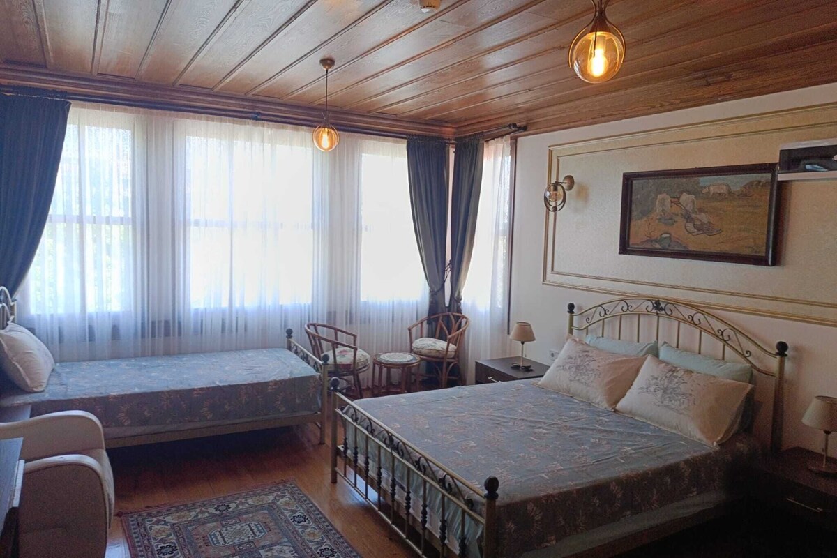 A room with a bed, a window seat, a chair, a rug, and a painting on the wall.