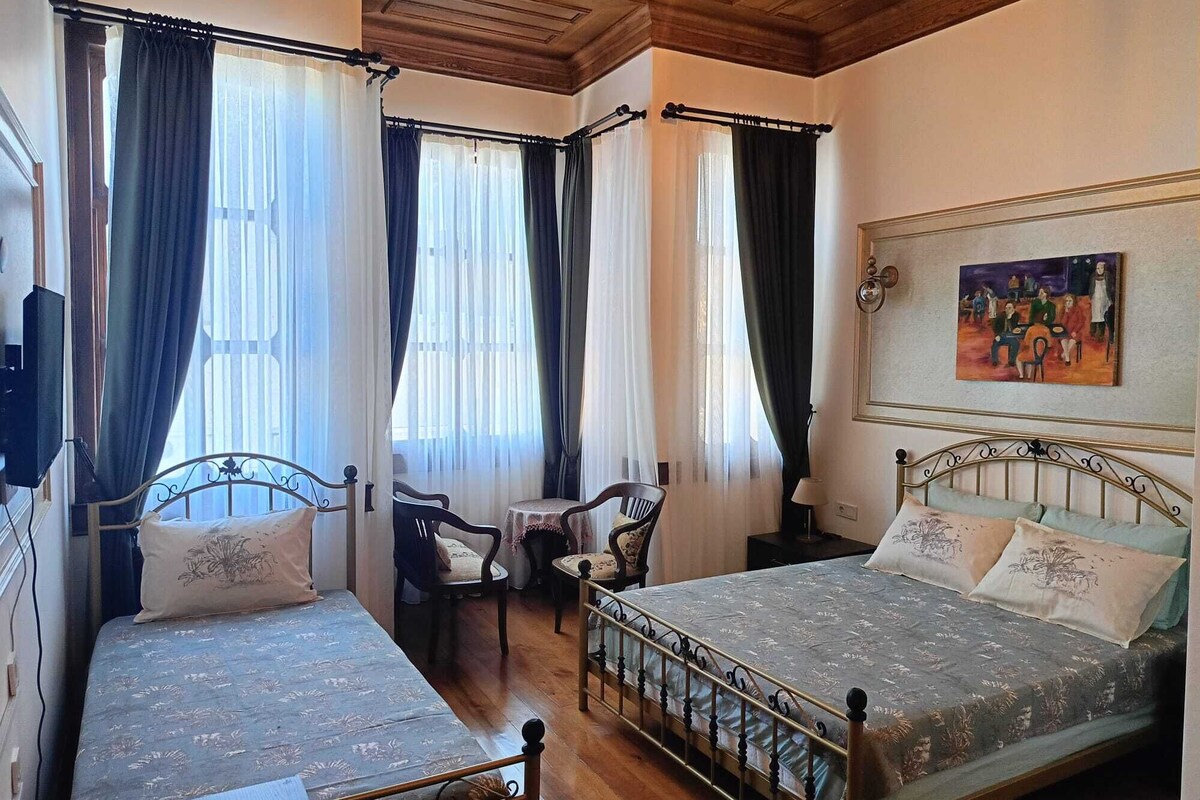 A room with two beds, a small table, and a chair. There is a painting on the wall.