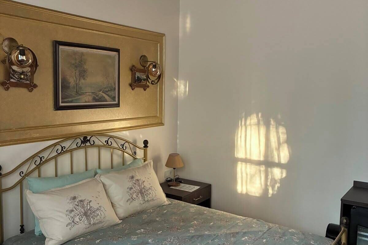 A bedroom with a bed, nightstands, a lamp, a framed picture, and a window casting a shadow.
