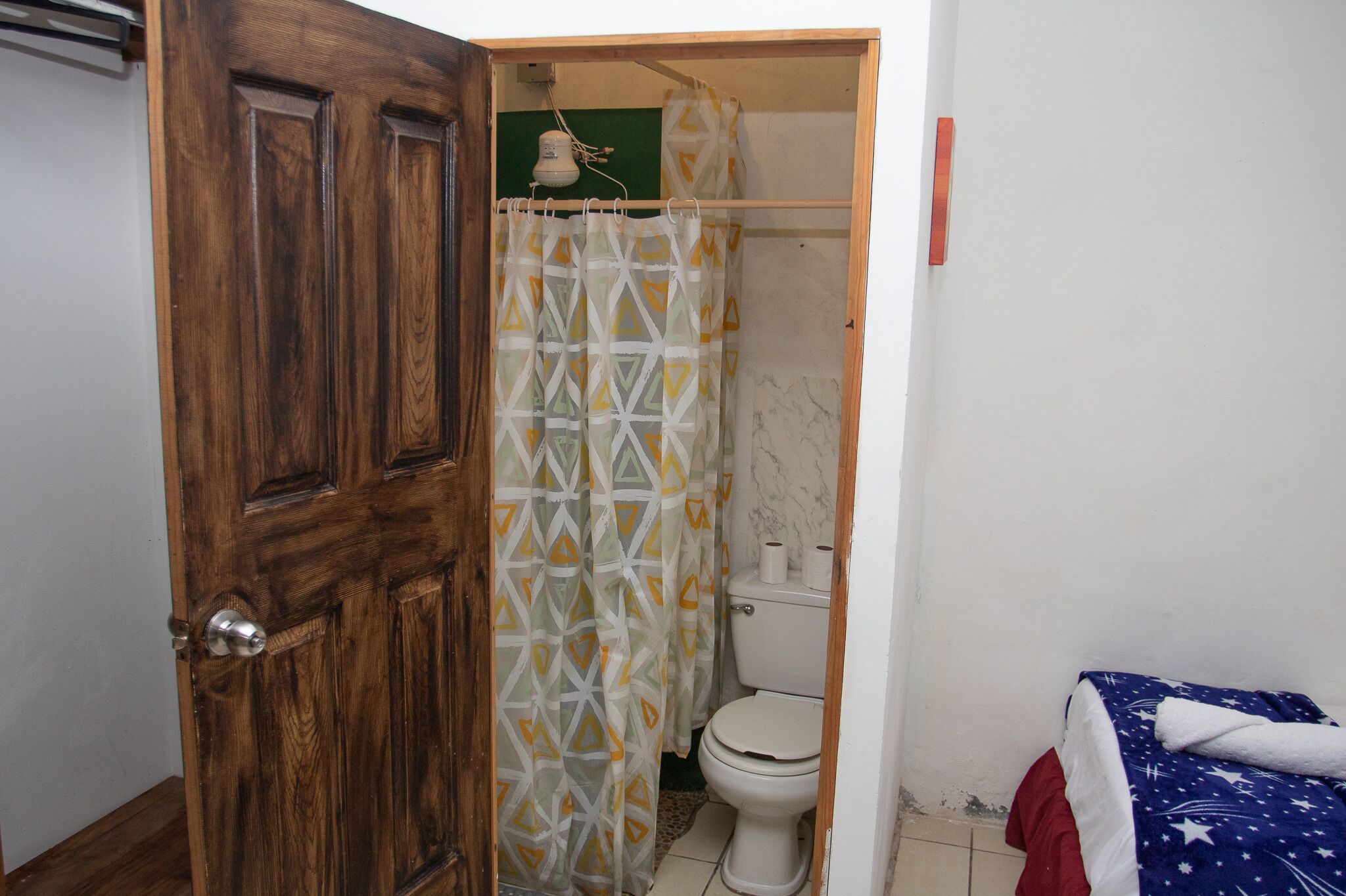 Ein Badezimmer mit Holztür, Duschvorhang, Toilette und Bett mit einem Bettbezug mit Sternenmuster.