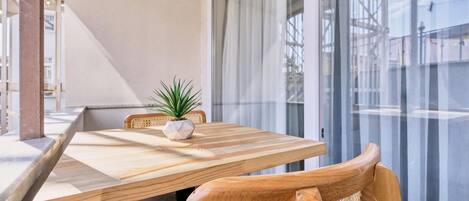 Un comedor con una mesa y sillas de madera, una planta en maceta y vistas a través de un ventanal.