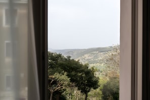 Blick durch ein Fenster auf eine hügelige Landschaft.
