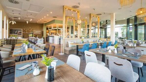 En modern restaurang med högt i tak, hängande lampor och en variation av sittplatser, inklusive bord och avskilda sittgrupper.