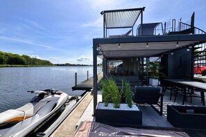 A modern outdoor deck with a dining area, a boat, and a view of the water.