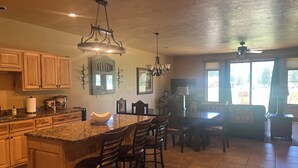 A kitchen with granite countertops, wooden cabinets, a central island with bar stools, pendant lighting, and a ceiling fan. - 3-bedroom townhome on Golf Course, Perfect Basecamp for Adventure or Relaxing (South Fork)